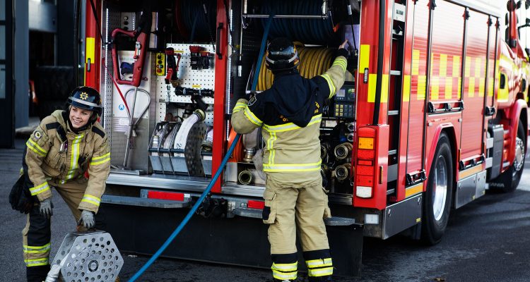 Två brandmän jobbar vid baksidan på en brandbil.