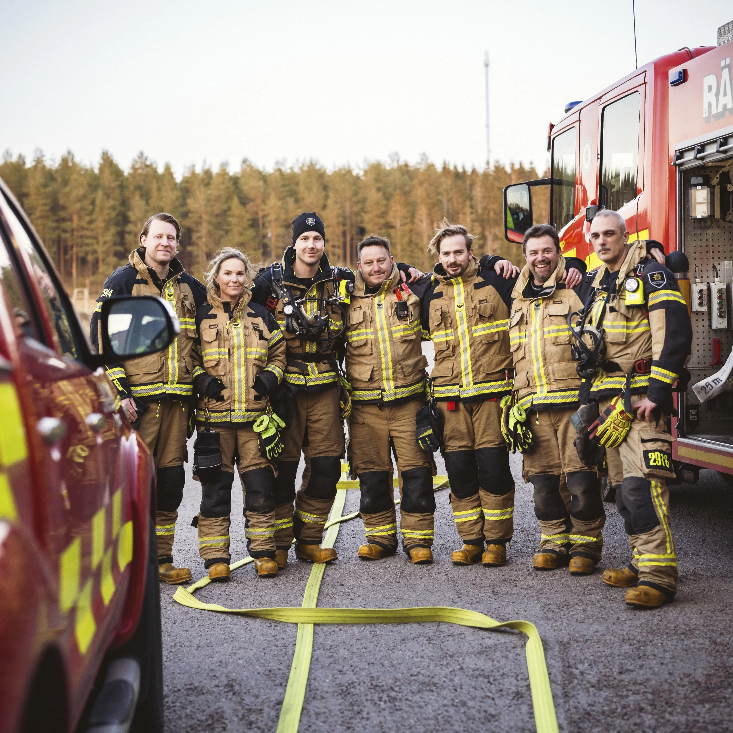 Sju brandmän som står samlade ute mellan två brandbilar