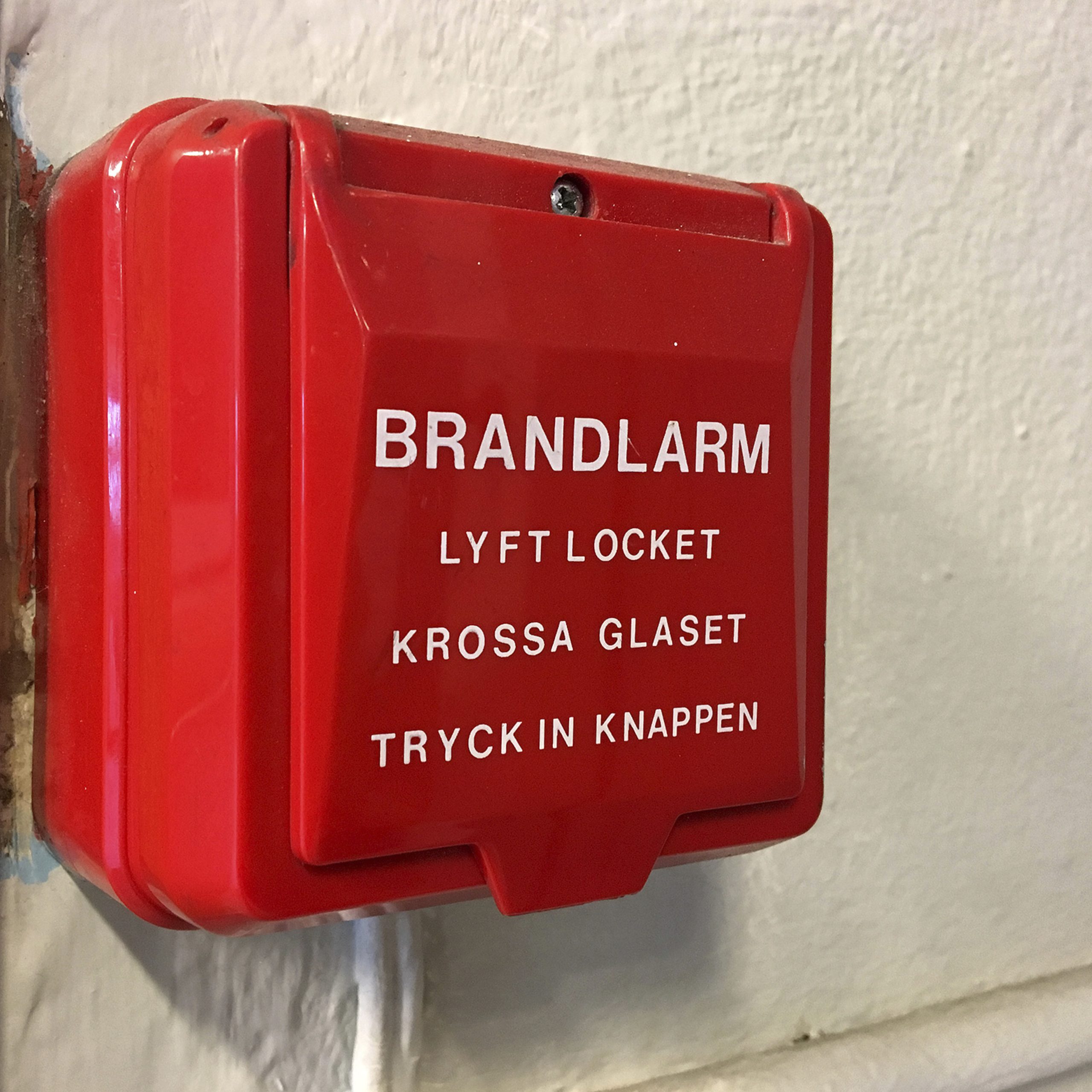 Ett automatlarm sitter monterat på en vägg. Det är en röd plastlåda och på står det "Brandlarm"