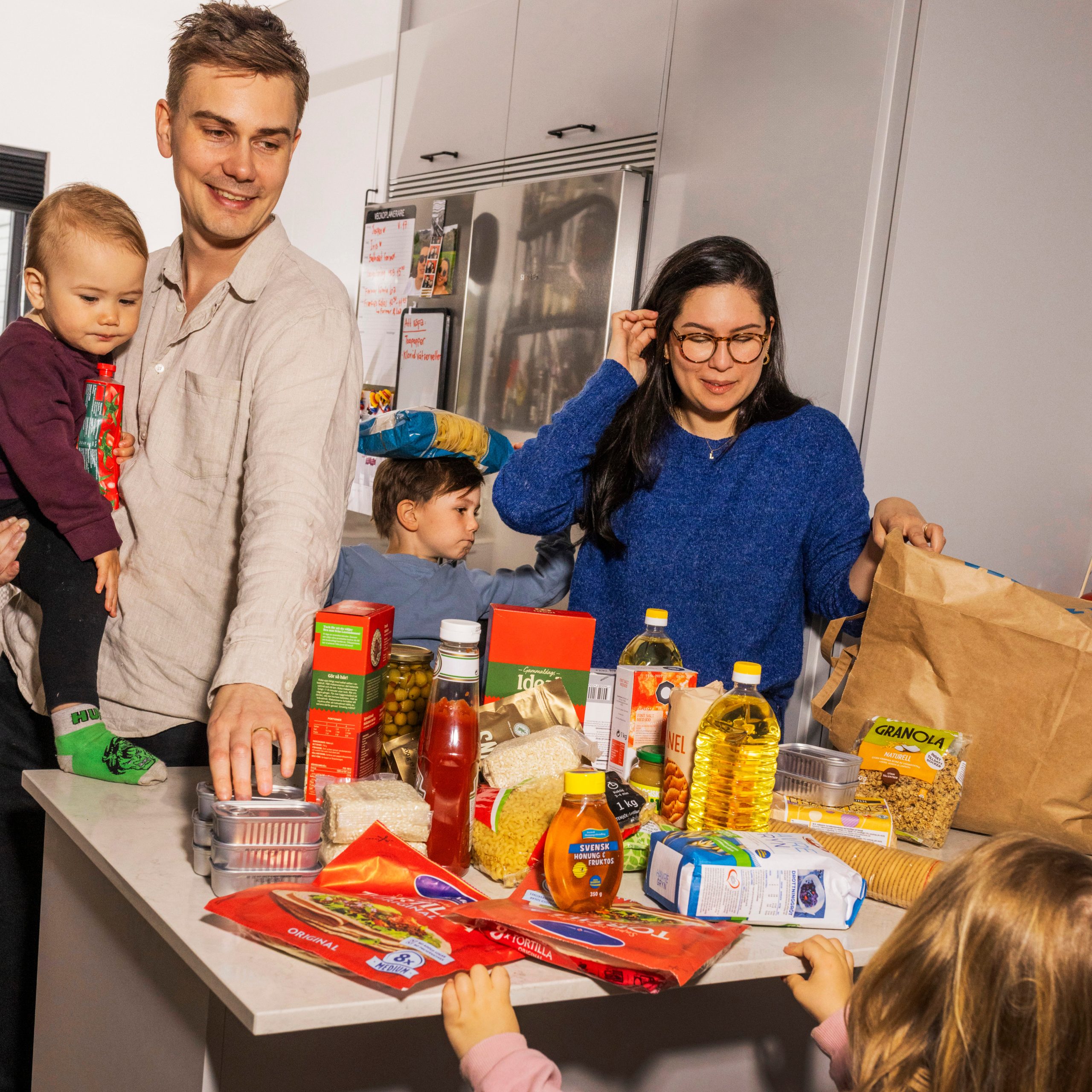På bilden syns en familj stå samlad runt ett bord fyllt med beredskapsmat så som konserver, pasta och olja.