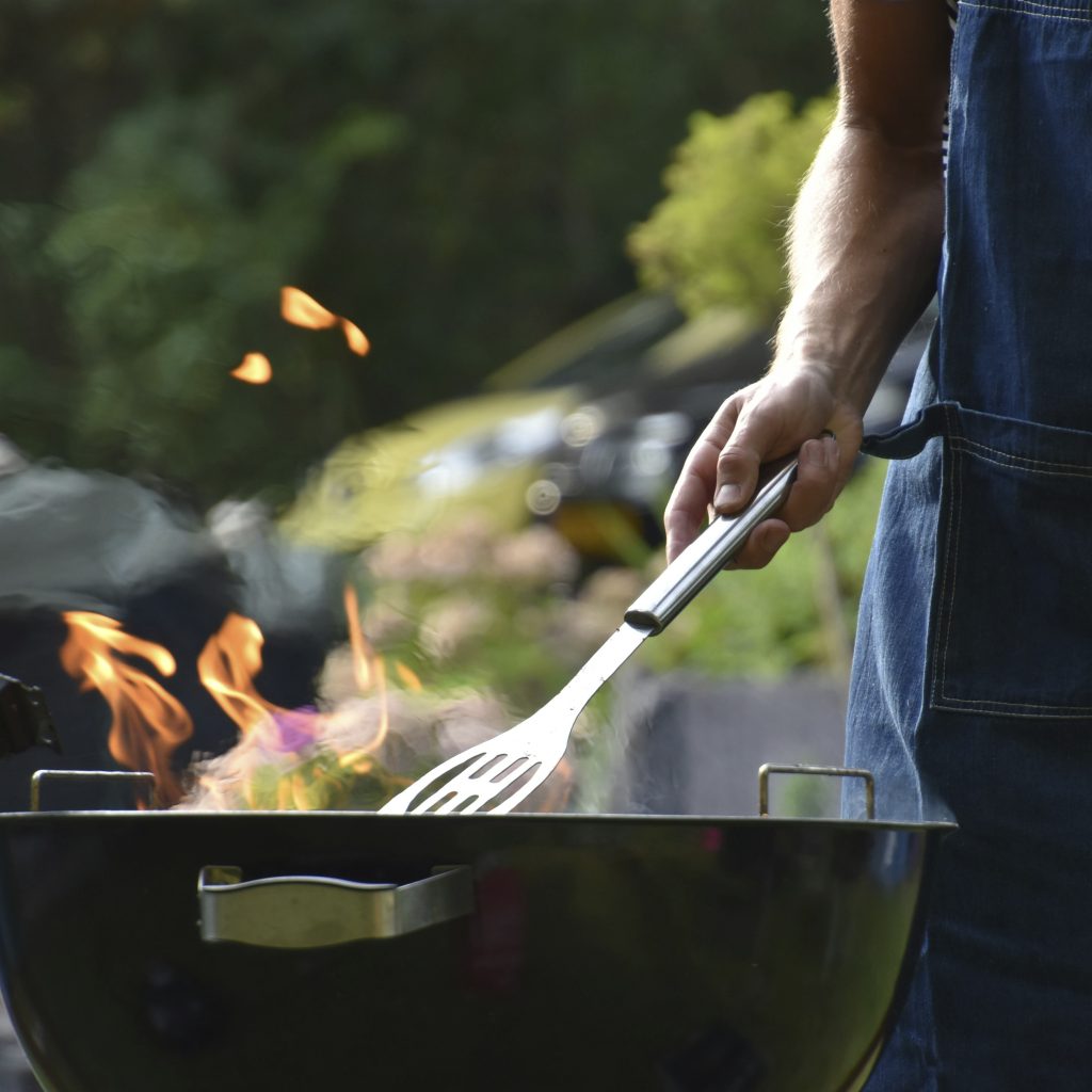En klotgrill brinner och en man står och överser den för att kunna börja laga mat.
