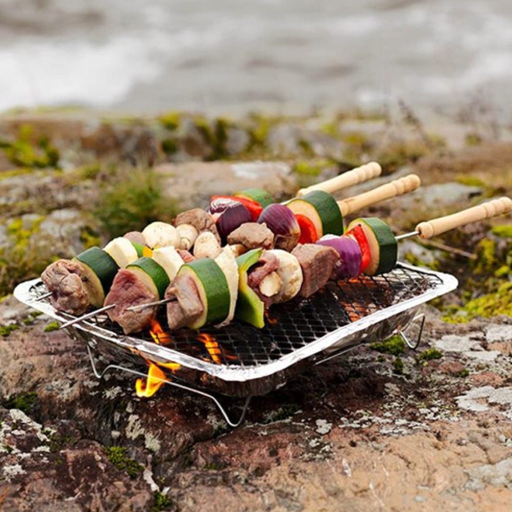 En engångsgrill står på en berghäll. på grillen ligger flera grillspett.