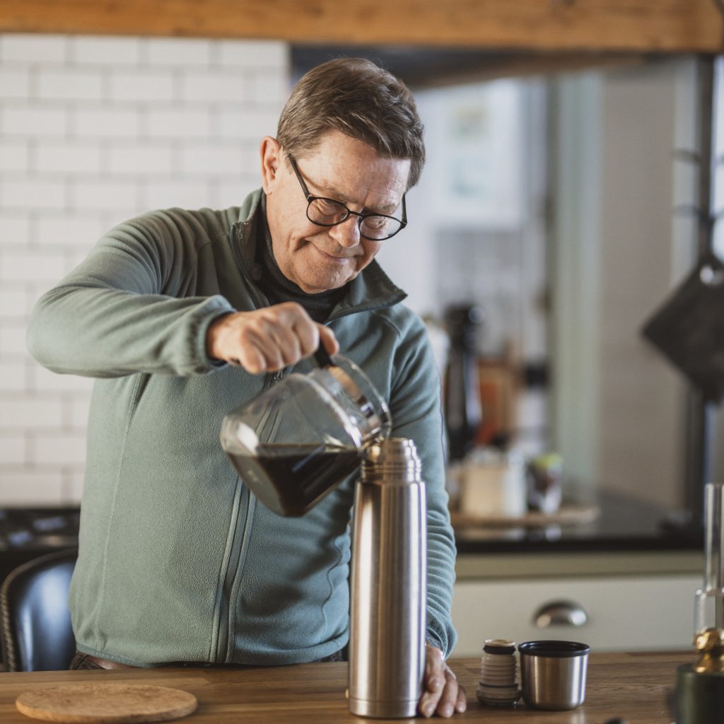 Man häller upp en kanna med kaffe i en termos.