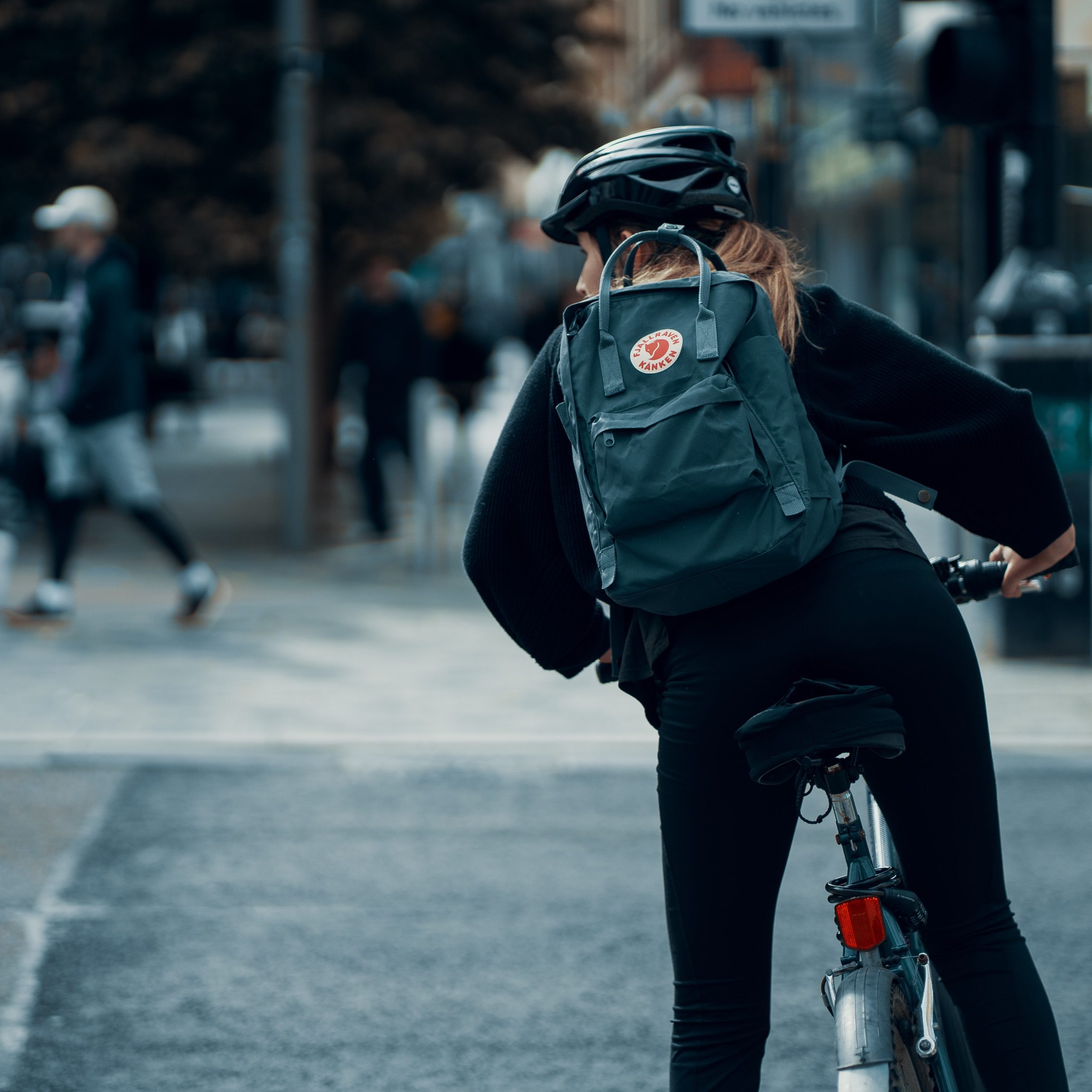 Cyklist har stannat till på cykelvägen för att titta till trafiken. Hon har cykelhjälm och ryggsäck på sig.