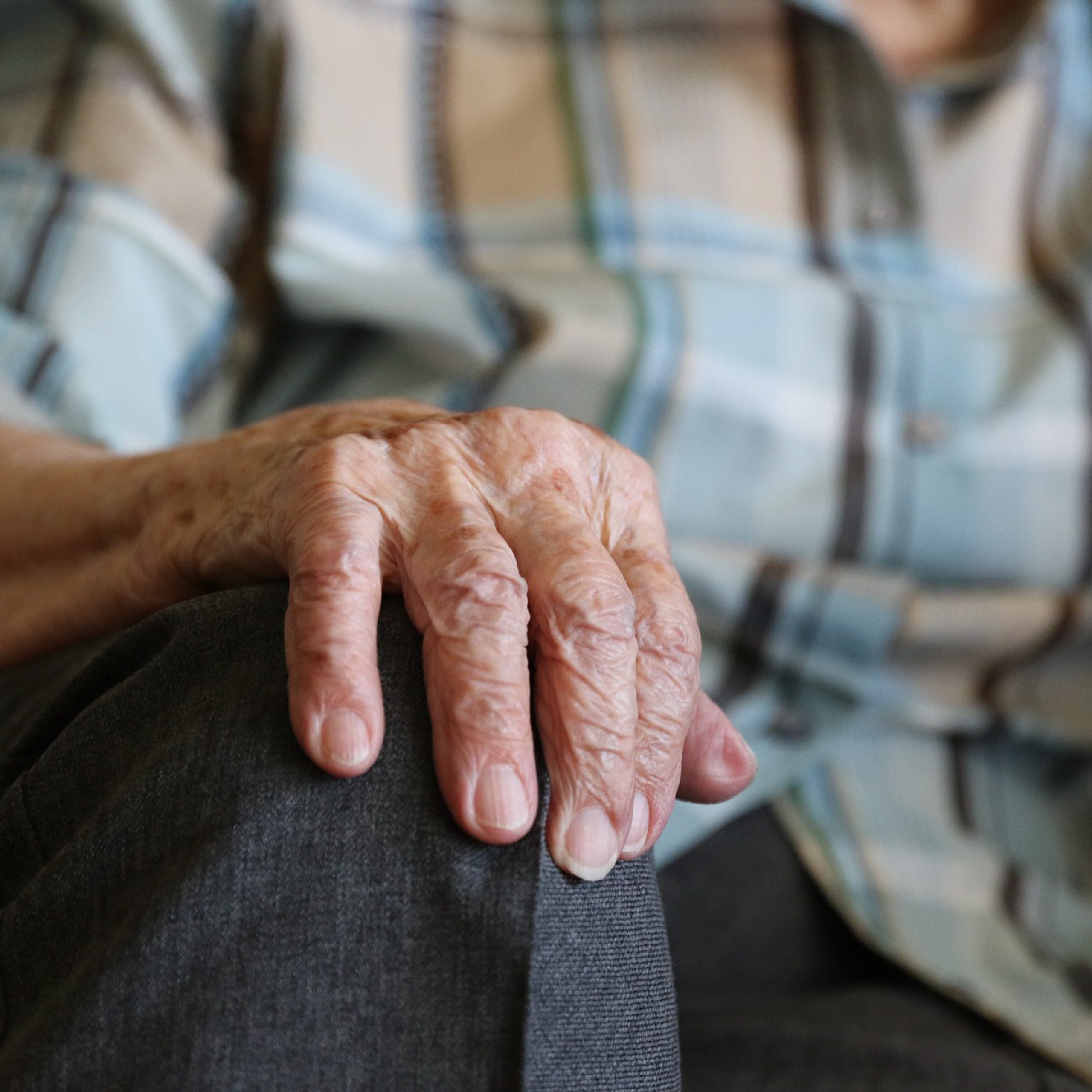 En äldre persons hand vilar på ett knä. Personen sitter ner.