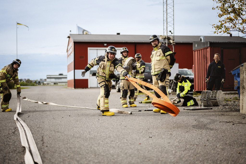 En grupp brandmän rullar ut slang under en övning.